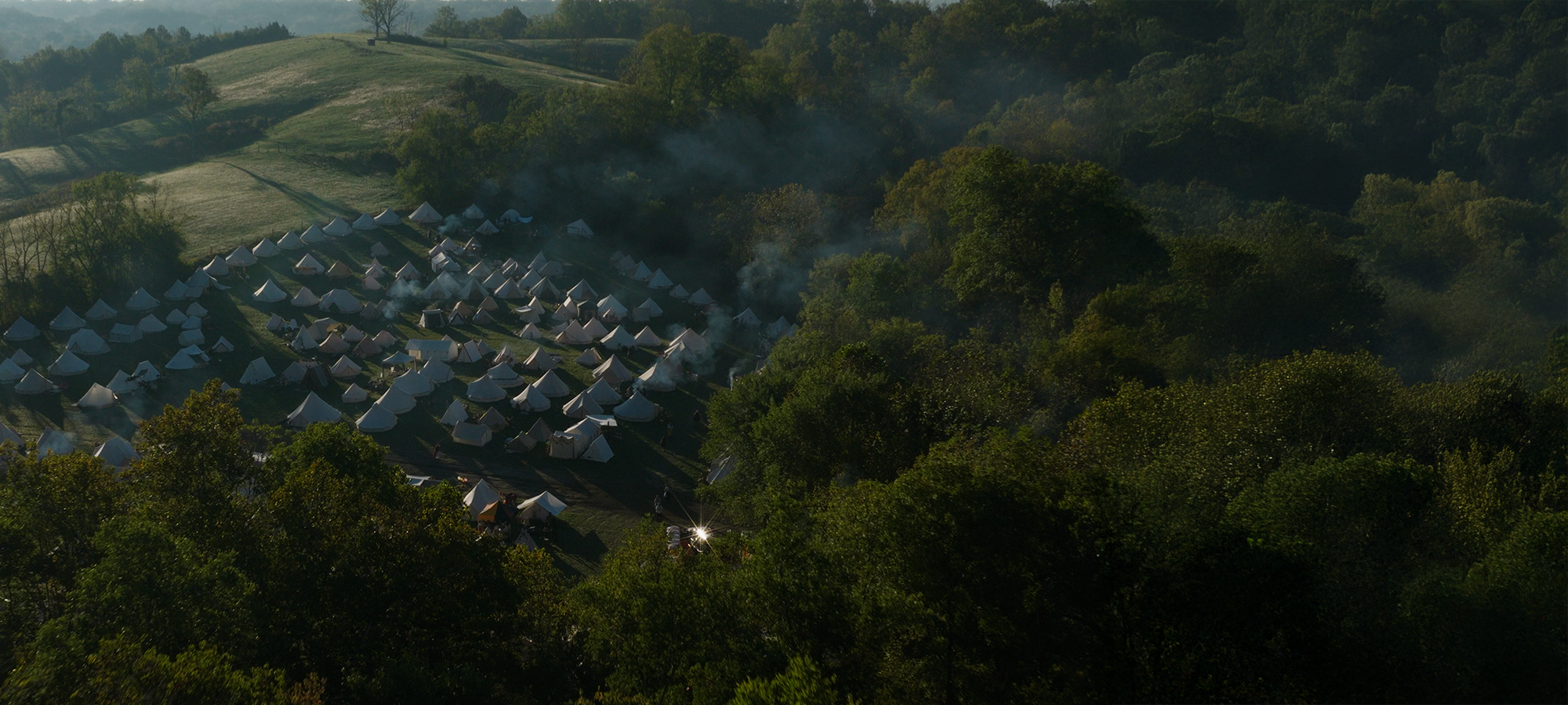 Tents camped in a forested area with misty hills in the background