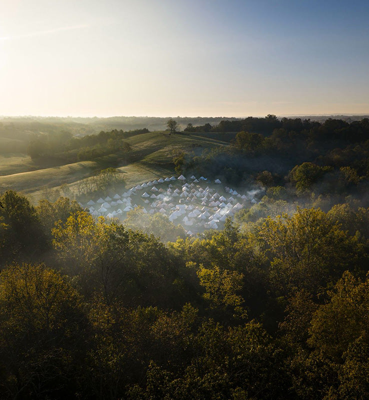 Aerial view of a forested area with a camping ground in the distance.