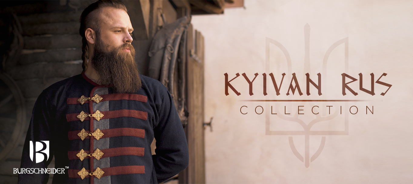 Das Model trägt den dunkelblauen Rus Mantel Kosma mit roten und grauen Akzenten und Messingschließen. Die Aufschrift ist Kyivan Rus Collection.